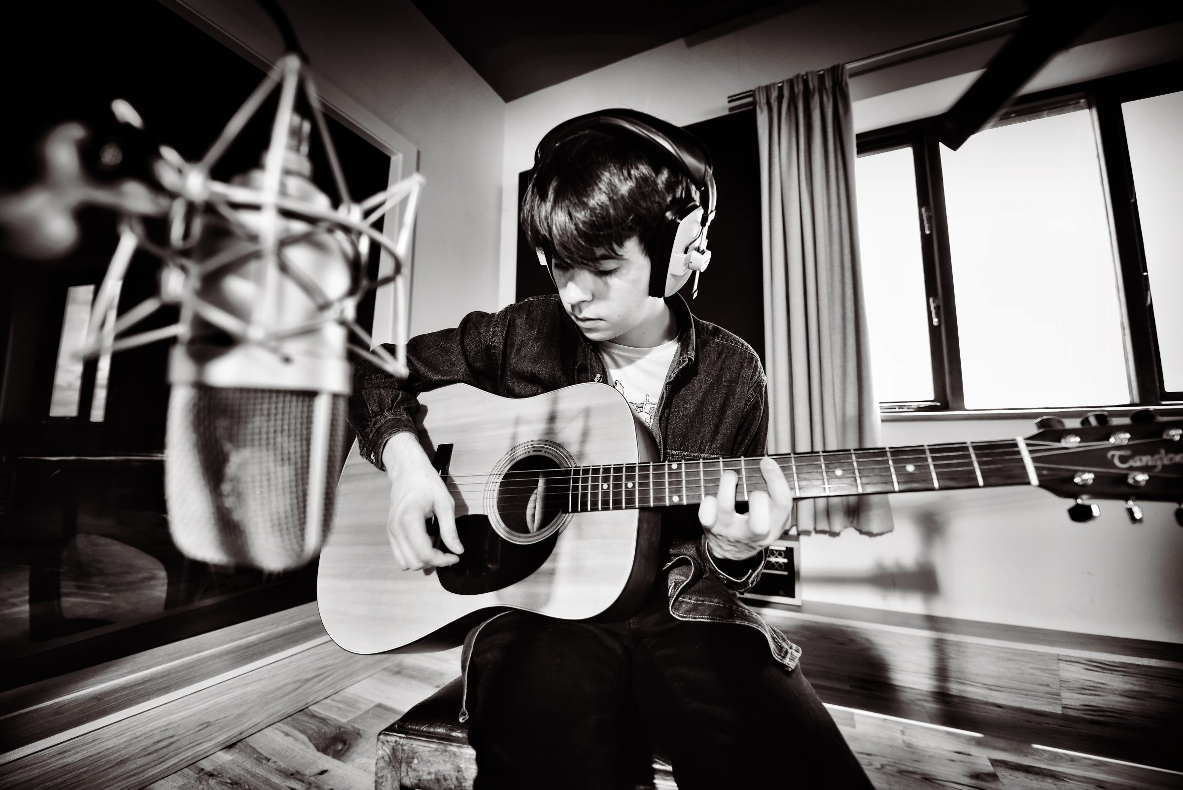 Black and white photo of an artist recording acoustic guitar with a microphone in the foreground