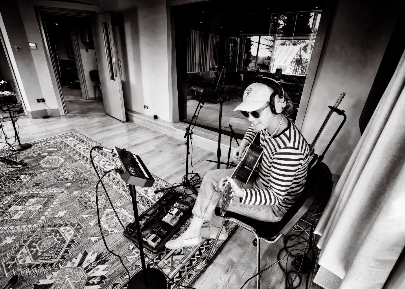 Black and white photo of an artist wearing a cap playing acoustic guitar in the control room