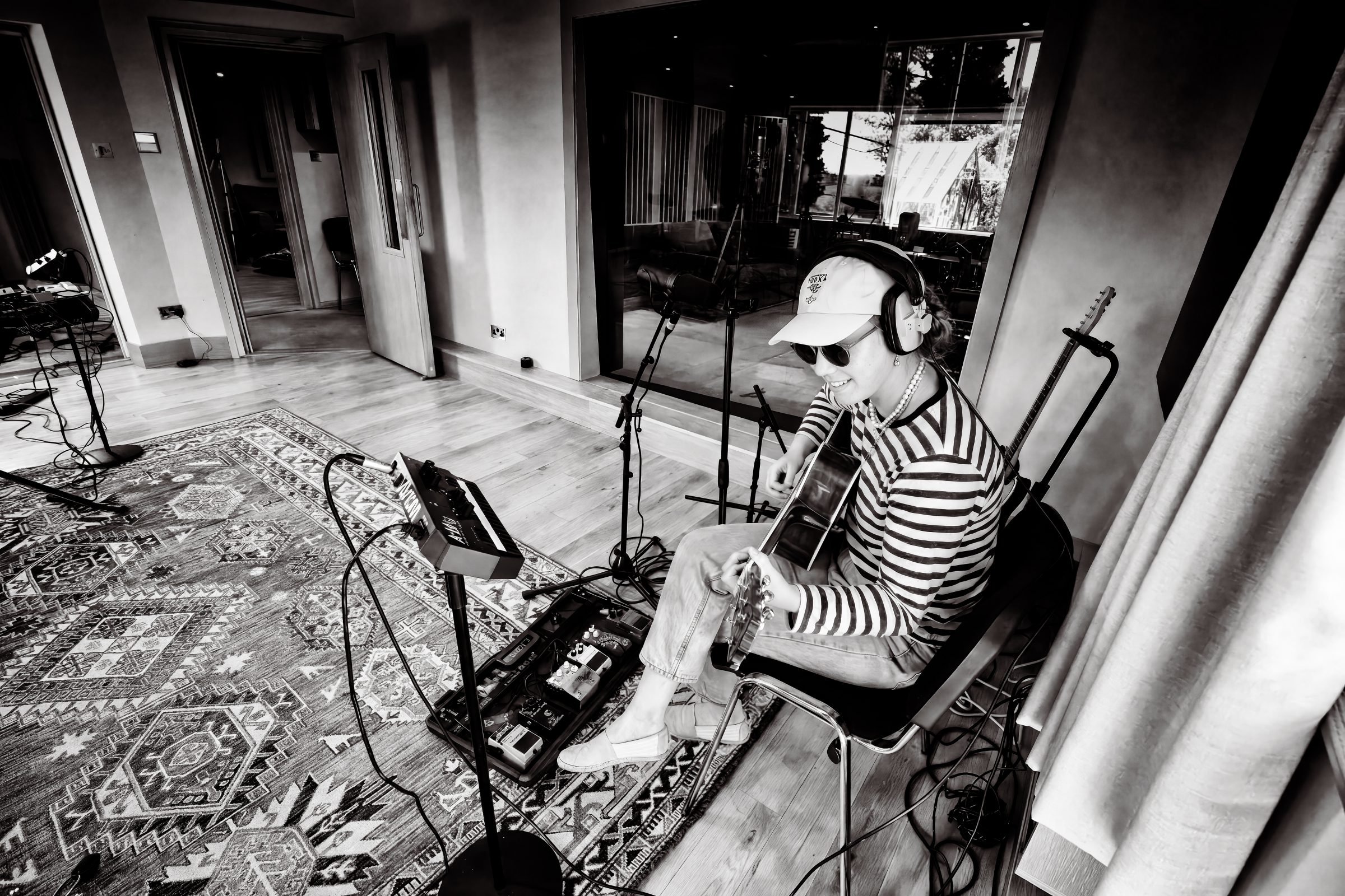 Black and white photo of an artist wearing a cap playing acoustic guitar in the control room