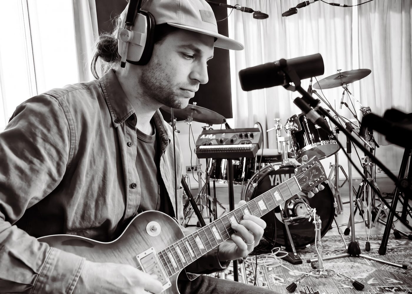 Black and white photo of a musician playing electric guitar with a drum kit behind